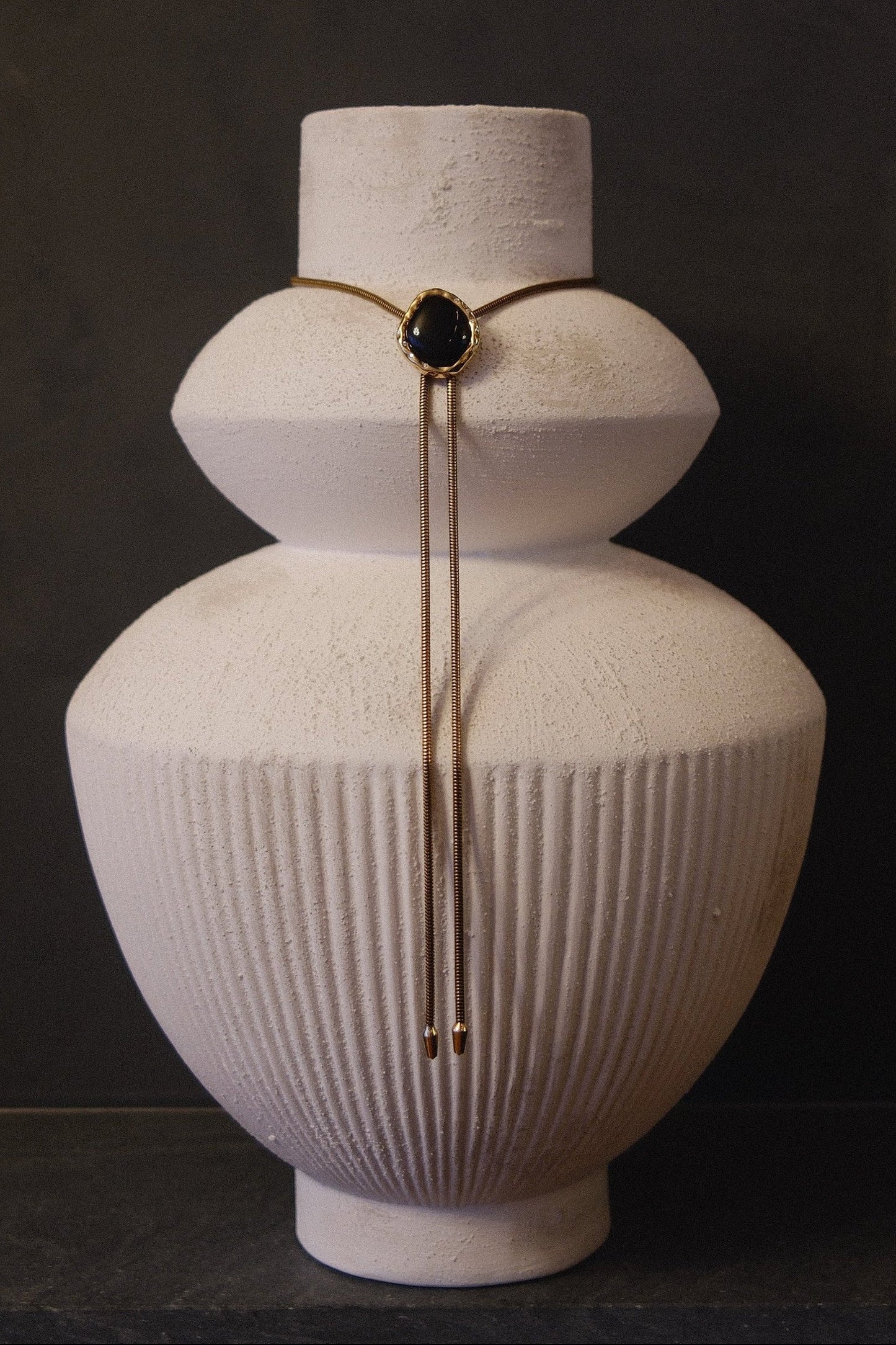 BOLOLA the LOLA necklace in onyx with gold plated chain and lab diamonds surrounding the stone featured on a white vase.