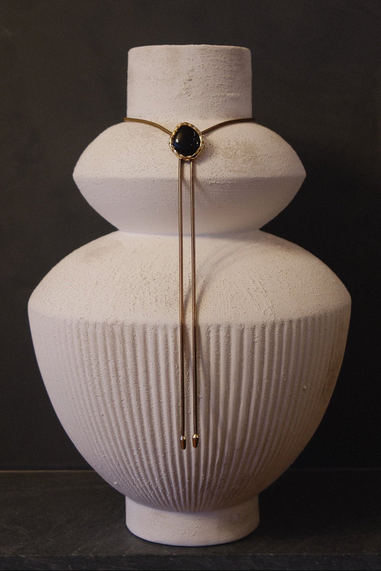 BOLOLA the LOLA necklace in onyx with gold plated chain and lab diamonds surrounding the stone featured on a white vase.