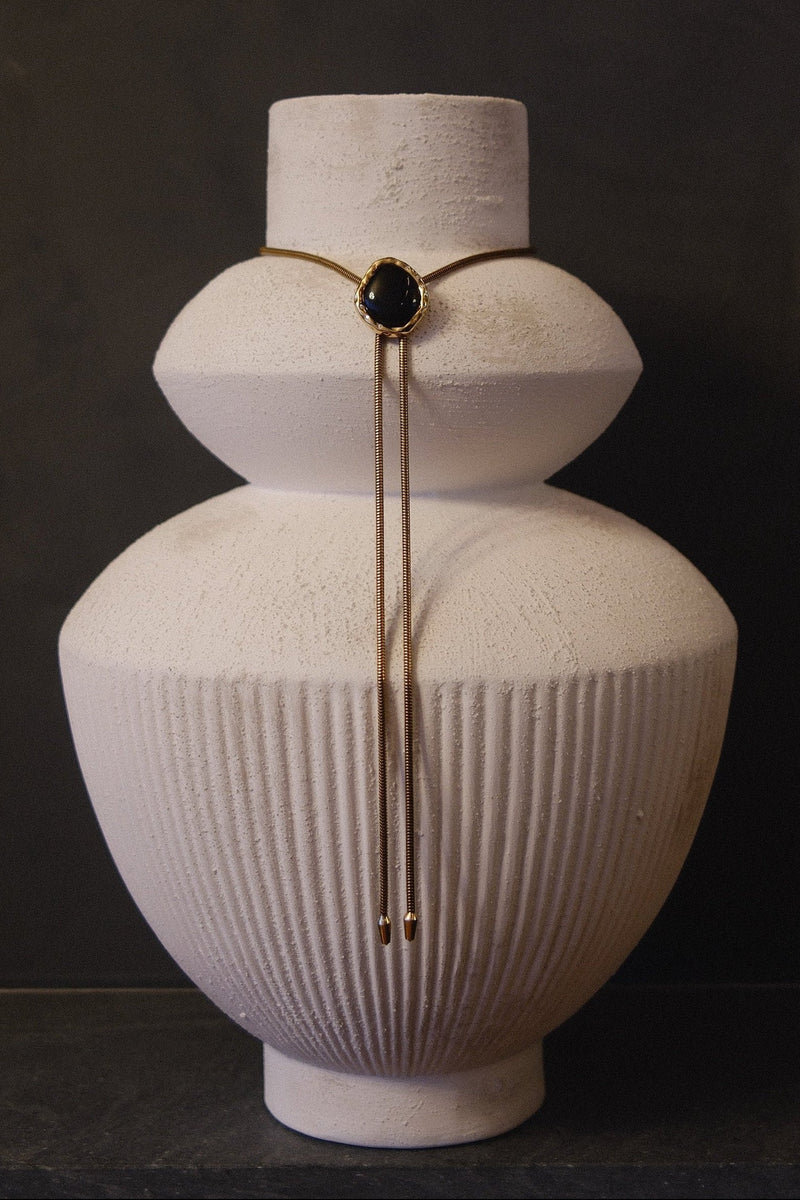 BOLOLA the LOLA necklace in onyx with gold plated chain and lab diamonds surrounding the stone featured on a white vase.