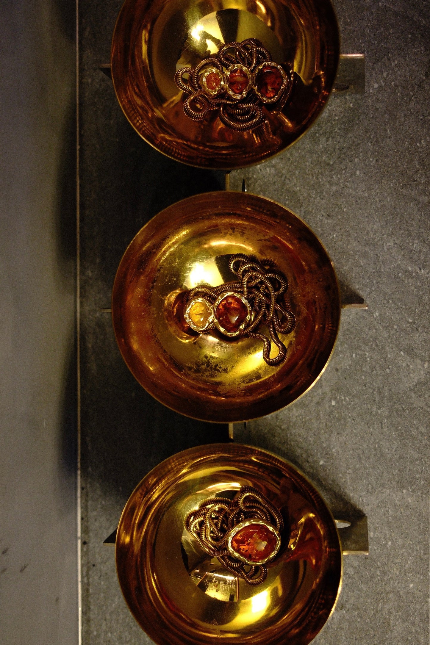 three gold bowls with amber and gold bolola necklaces inside them