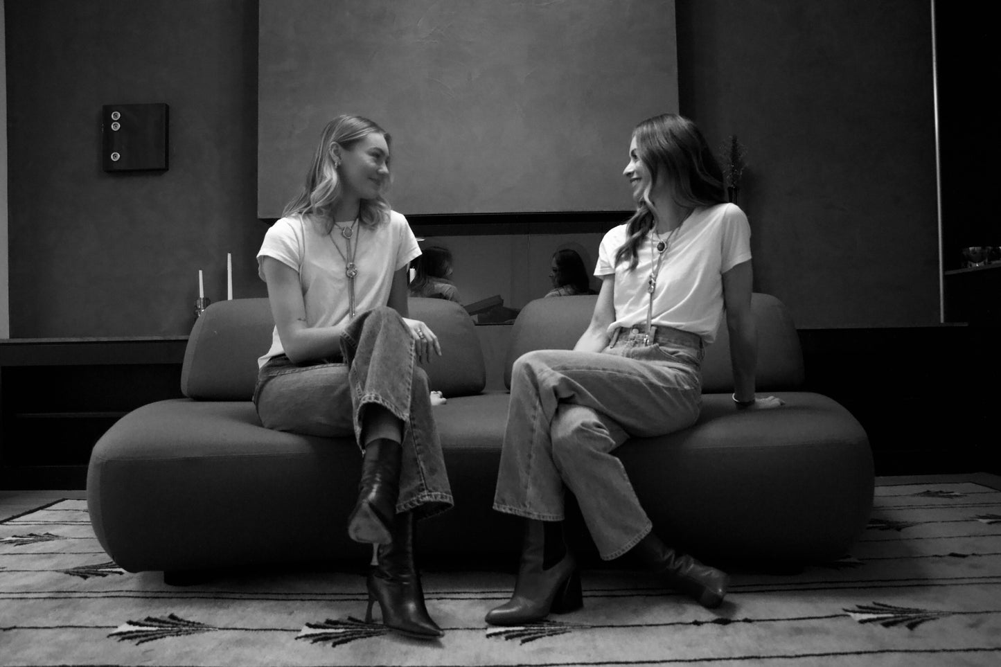 The founders of BOLOLA, Martha and LOLA sitting on a couch smiling at each other. 