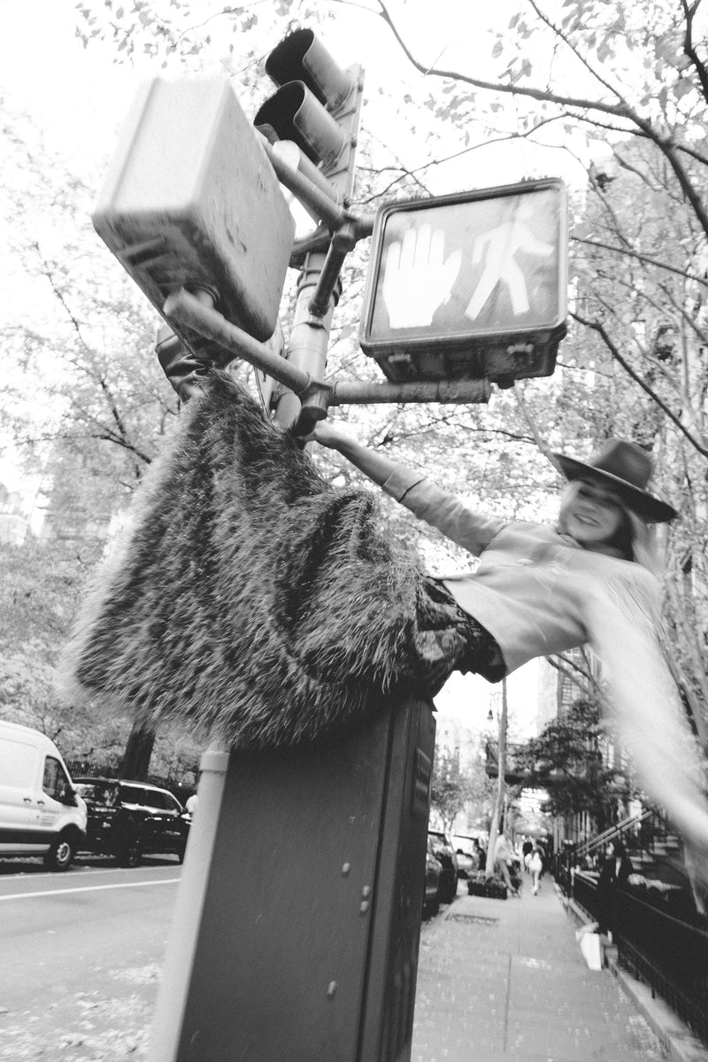 Person reaching out to touch a traffic light with a hat on a city street.