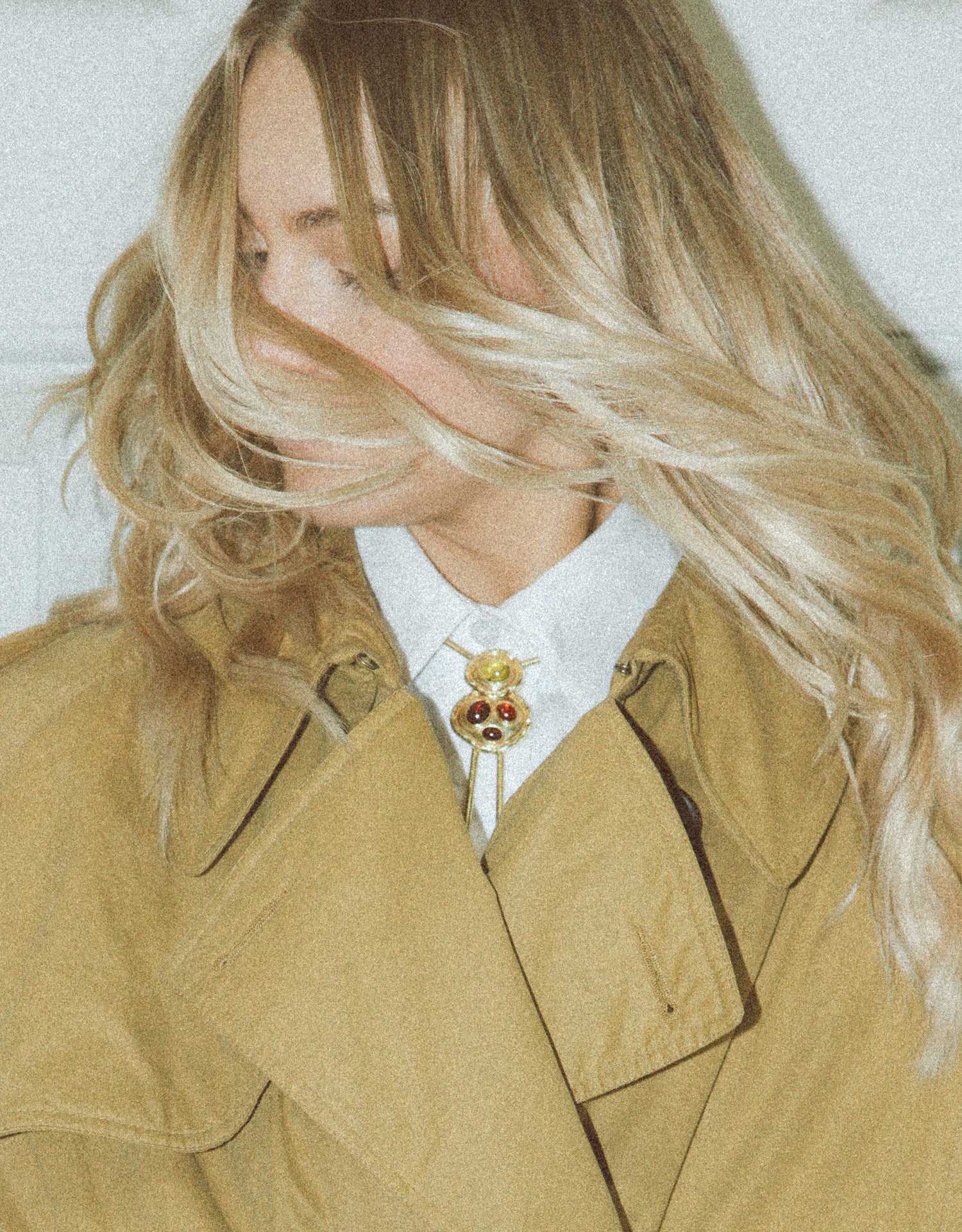 Model wearing the BOLOLA The Blythe necklace with garnet and tourmaline in gold plated metal, styled with a collared shirt and a beige trench coat. 