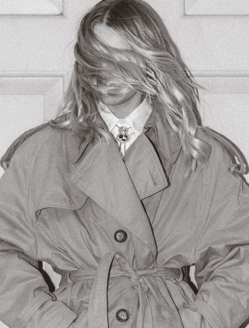 Person wearing a trench coat with a blurred face on a light background